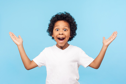 No way, I can't believe! Portrait of funny amazed preschool boy keeping hands up in astonishment, looking surprised and sarcastic at camera, excited shocked by sudden news. studio shot blue background