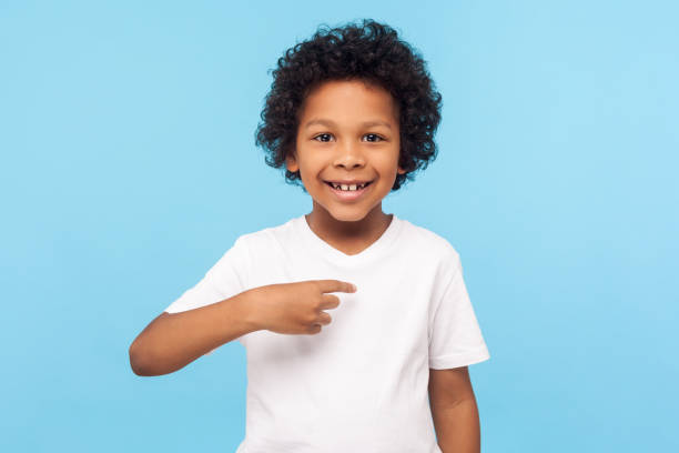 eu sou assim. retrato de menino feliz pré-escola encaracolado em camiseta alegremente olhando para a câmera e apontando para si mesmo - child excitement awe fun - fotografias e filmes do acervo