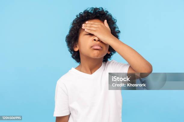 Facepalm Portrait Of Forgetful Upset Little Boy With Curls Covering Face With Hand And Expressing Sorrow Stock Photo - Download Image Now