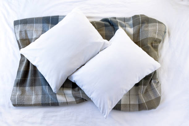 Two blank white pillows on a white bed with blue/gray tartan throw - pillowcase flat lay mockup