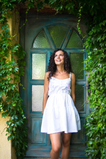 Young smiling woman standing in front of her stylish decorated house with creeper plant in summer.