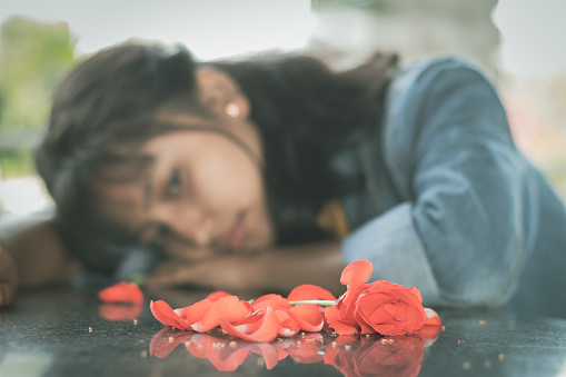 Selective focus on red rose lonely young teenager - concept of love breakup or broken heart.