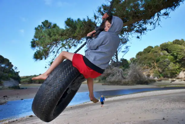 A child swings on a swing made from an old tyre by a coastal estuary in winter.