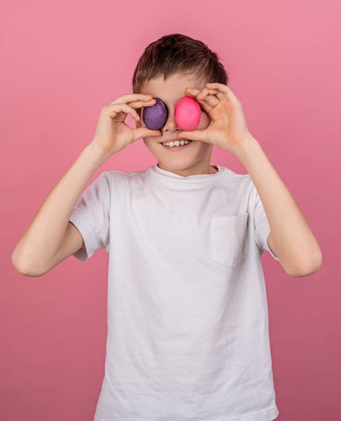 istock Smiling boy covering eyes with colorful eggs isolated on pink bakground 1204549268