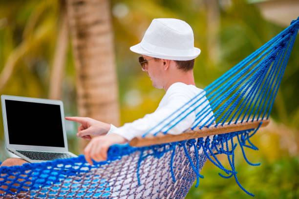 istock Young man with laptop at hammock on tropical vacation 1204553880