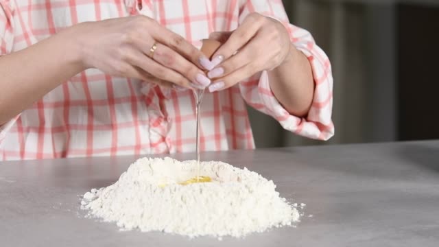Woman adds an egg to a flour mound