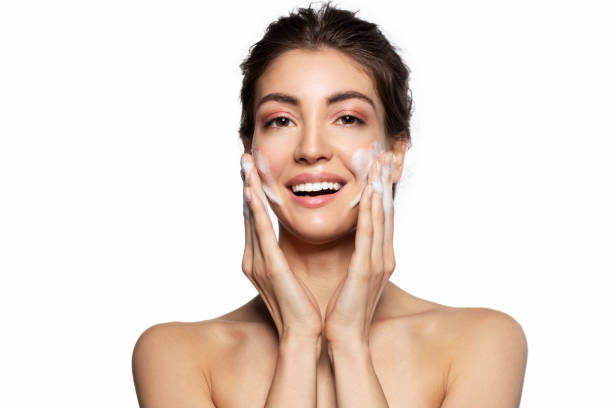 smiling young woman cleaning face with soap foam - facial cleanser imagens e fotografias de stock