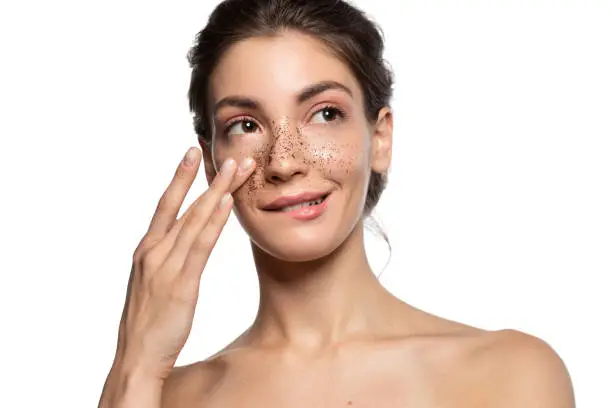 Portrait of smiling woman applying cosmetic facial skin scrub, natural coffee mask.