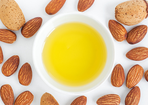 Small white bowl with almond oil. Top view, copy space, white background