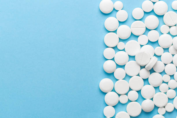 istock scattered white pills on a blue table. Layout for special offers such as advertising or other ideas. The concept of medicine, pharmacy and healthcare. Space for copy. 1204572765