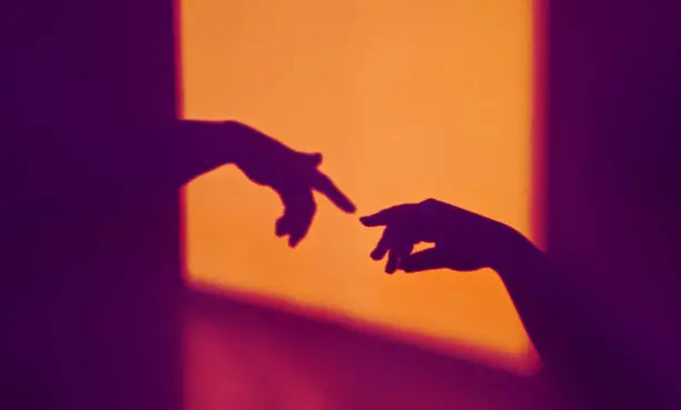 Abstract shadow silhouette of gesture touch by humans palms from sunbeam on wall during posing wrist and fingers in contrasting colors. Creation of Adam metaphor by Michelangelo