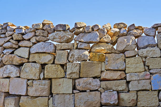 Limestone wall of brickwork with cracked boulders against blue sky Limestone wall of brickwork with cracked boulders against blue sky background. Natural build texture with copy spac fortified wall stock pictures, royalty-free photos & images