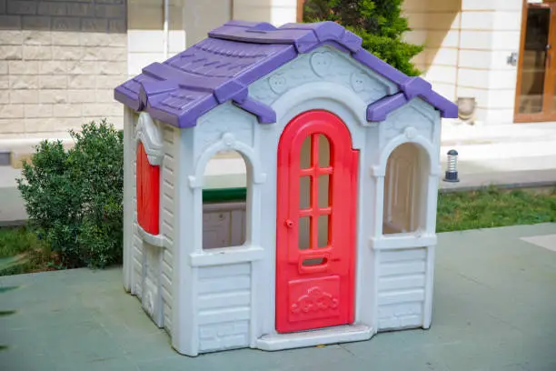 plastic colorful house . Entertainment area.kids playhouse in the entertainment center. Plastic children play house . Green floor. Joy and fun. Playing games.with red door and red window .Game house .