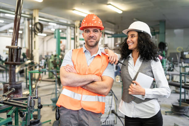 istock Smiling businesswoman and foreman standing in factory, using tablet 1204573452