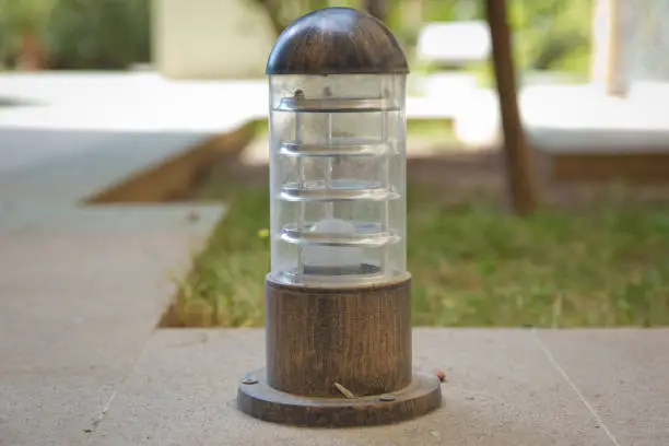 Lighting ground lamp street mounted on a green lawn in a park . Lamp set on a wood on a high ground . small lantern in a garden on the ground