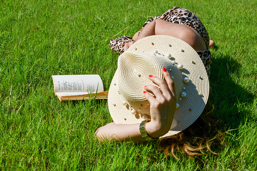 Woman lying on the grass is reading a book.