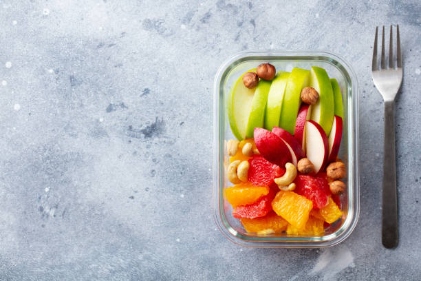 fruits salad and nuts in a glass container. healthy eating. grey background. copy space. top view. - lunch box lunch red apple imagens e fotografias de stock