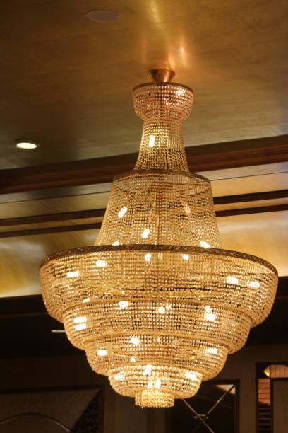 istock Bulbs shine brightly from a golden tiered chandelier from a ceiling 1204583400