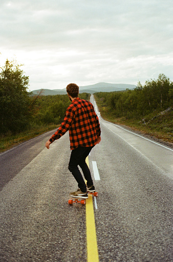 Young Caucasian man in checked shirt  longboarding  on the road in Finland