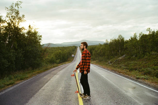 Young Caucasian man in checked shirt  longboarding  on the road in Finland