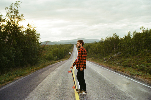 Young Caucasian man in checked shirt  longboarding  on the road in Finland