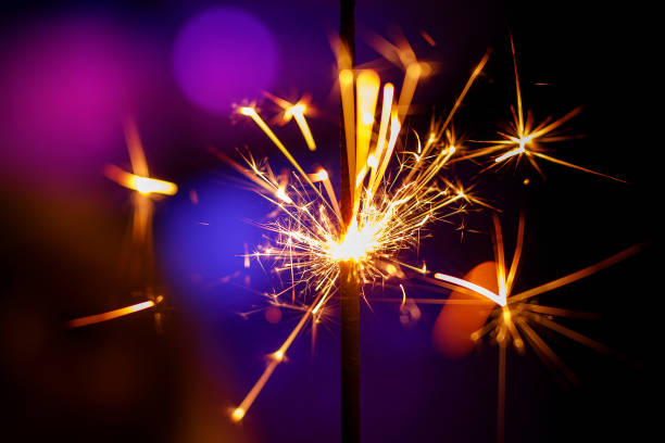 istock Glittering burning sparkler on purple and blue background. 1204594242