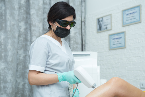 Beautician removes hair from a female leg with a laser. Laser depilation treatment in beauty spa.