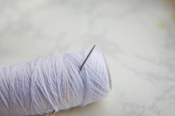 Needle on white thread white background. White bobbin with needle isolated on white .Close up sewing thread with an embroidery needle. Crafts and DIY concepts .