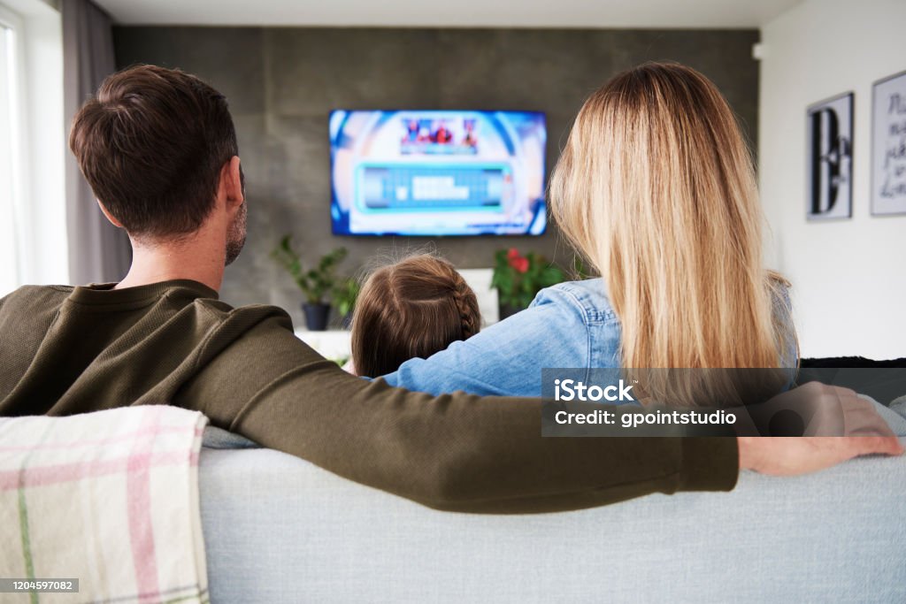 Rear view of family watching tv in living room Watching TV Stock Photo