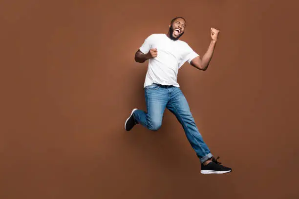 Photo of Full length body size photo of cheerful positive excited crazy ecstatic overjoyed man rejoicing about having bought new discounted jeans denim footwear white t-shirt jumping running isolated pastel color background