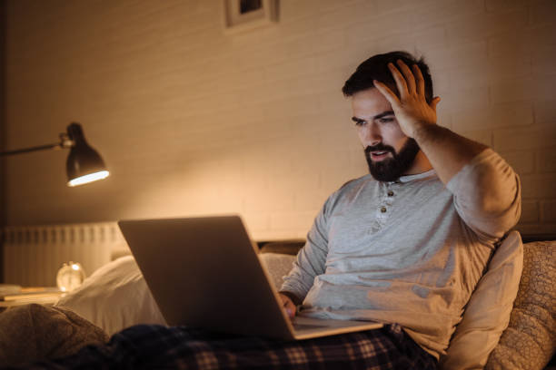 istock Upset young man working late in bed on a laptop 1204598312