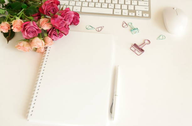 istock flat lay top view women's office desk on  white background selective focus. Female workspace with laptop, beautiful pink roses flowers in a vase, gift box, accessories, notebook mock up, glasses. 1204599344