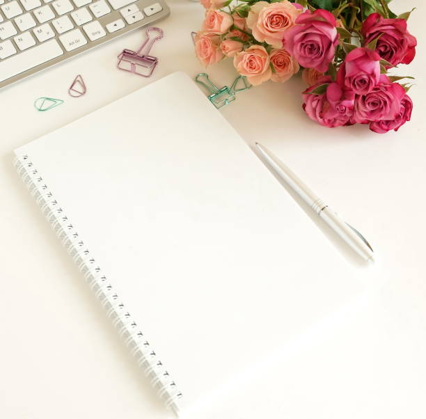 istock flat lay top view women's office desk on  white background selective focus. Female workspace with laptop, beautiful pink roses flowers in a vase, gift box, accessories, notebook mock up, glasses. 1204599743