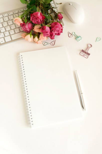 istock flat lay top view women's office desk on  white background selective focus. Female workspace with laptop, beautiful pink roses flowers in a vase, gift box, accessories, notebook mock up, glasses. 1204600199