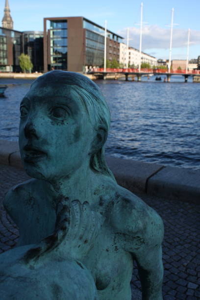 Copenhagen, Denmark: August 16, 2016 - The Black Diamond Mermaid Statue in Copenhagen. The Black Diamond is a modern waterfront extension to the Royal Danish Library's old building on Slotsholmen in central Copenhagen.This bronze mermaid statue was unveiled on May 5th in 2009 by the Royal Library on the wharf in front of the Royal Library building, known as The Black Diamond (Den Sorte Diamant).