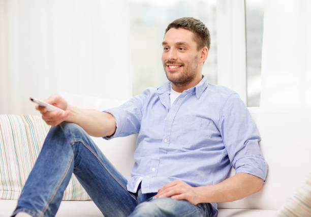 istock smiling man with tv remote control at home 1204603501