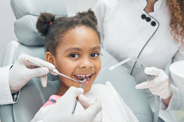 Happy afro kid on regular check up of teeth in dental clinic Happy afro american girl sitting in stomatologist chair with open mouth while professional dentist doing regular check up of teeth using dental probe and mirror. Female nurse assisting. pediatric dentistry stock pictures, royalty-free photos & images