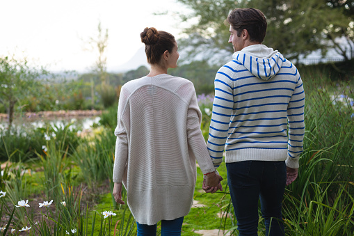 Rear view of a Caucasian couple holding hands and walking in the garden, looking at each other and smiling. Home and lifestyle weekend activities.