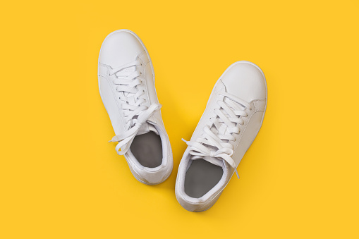 A pair of white sneakers on a yellow background in a top view
