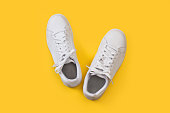 A pair of white sneakers on a yellow background