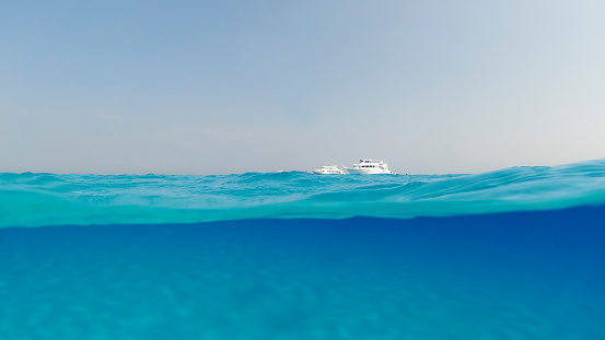 A yacht in the turquoise ocean is visible bottom, Underwater split shot photos