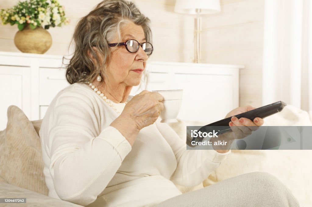 Una anciana con un control remoto de TV en la mano - Foto de stock de Adulto libre de derechos