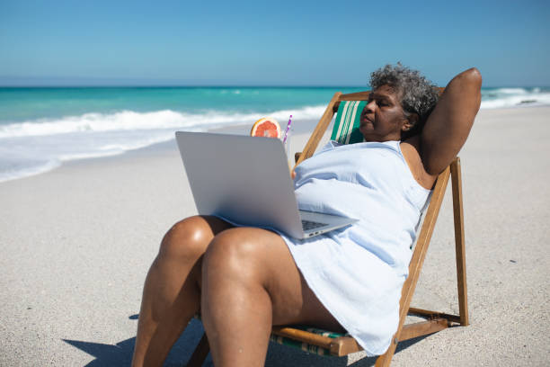 istock Old woman on laptop at the beach 1204620917