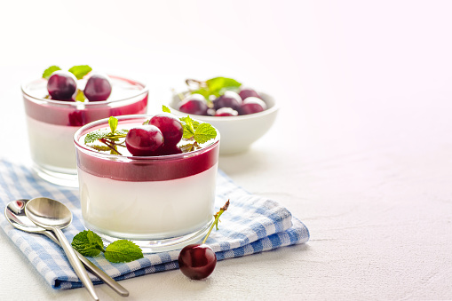 Traditional italian creamy dessert panna cotta. Dessert in a glass decorated with fresh cherry berries and red jelly and mint leaves. Ready to eat. Copy space and horizontal orientation.\