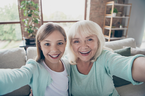 Closeup photo of two people white haired grandma small granddaughter, making selfies video call skype spending summer weekend together house indoors