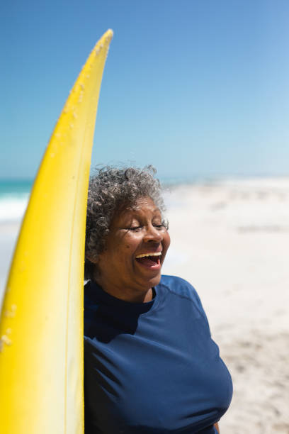 istock Old woman with a surfboard at the beach 1204623657