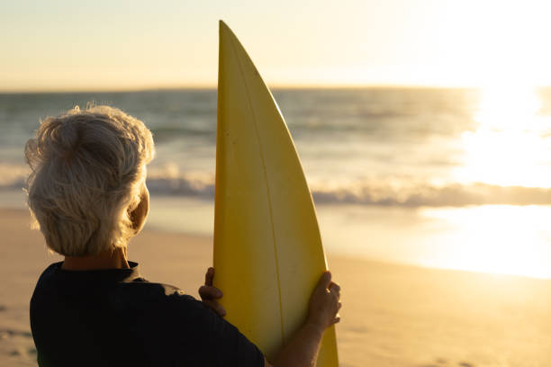 istock Old woman with a surfboard at the beach 1204628303