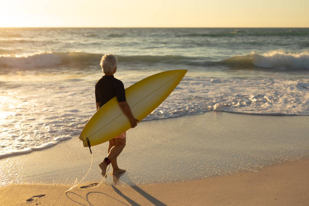 istock Old woman with a surfboard at the beach 1204628386