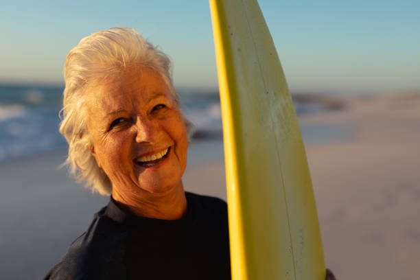 istock Old woman with a surfboard at the beach 1204628473