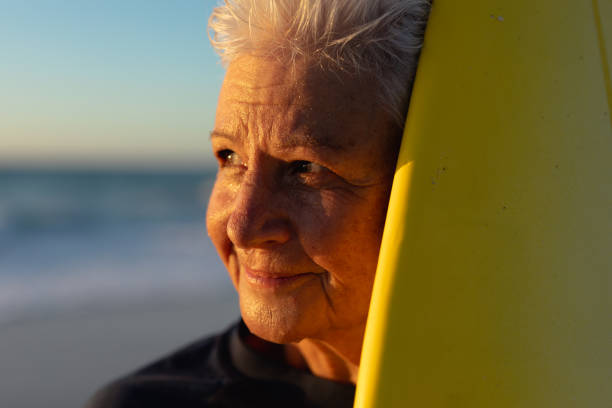 istock Old woman with a surfboard at the beach 1204628487